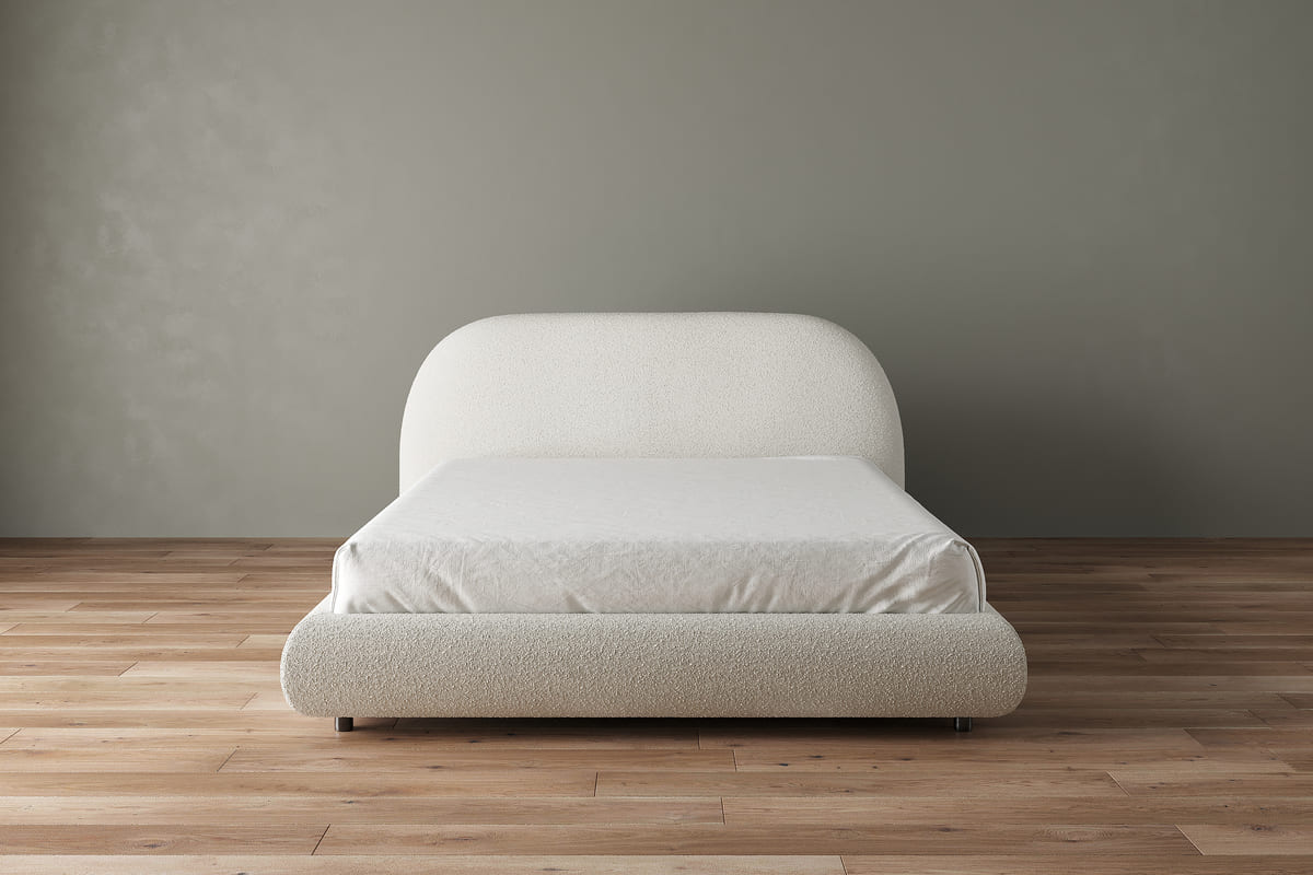White bed in a minimalistic room with a plain wall and wooden floor.