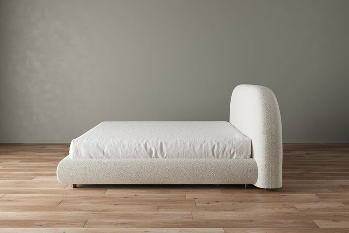 Beige upholstered bed against a plain wall on a wooden floor