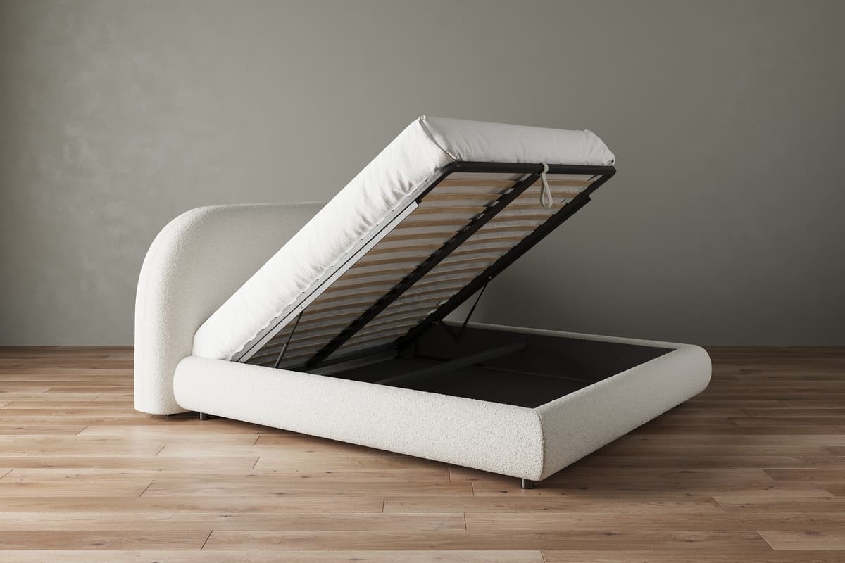 White upholstered bed with storage compartment on a wooden floor against a gray wall
