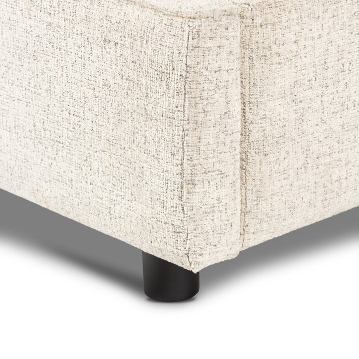 Close-up of a textured beige upholstered corner piece with a black leg on a white background