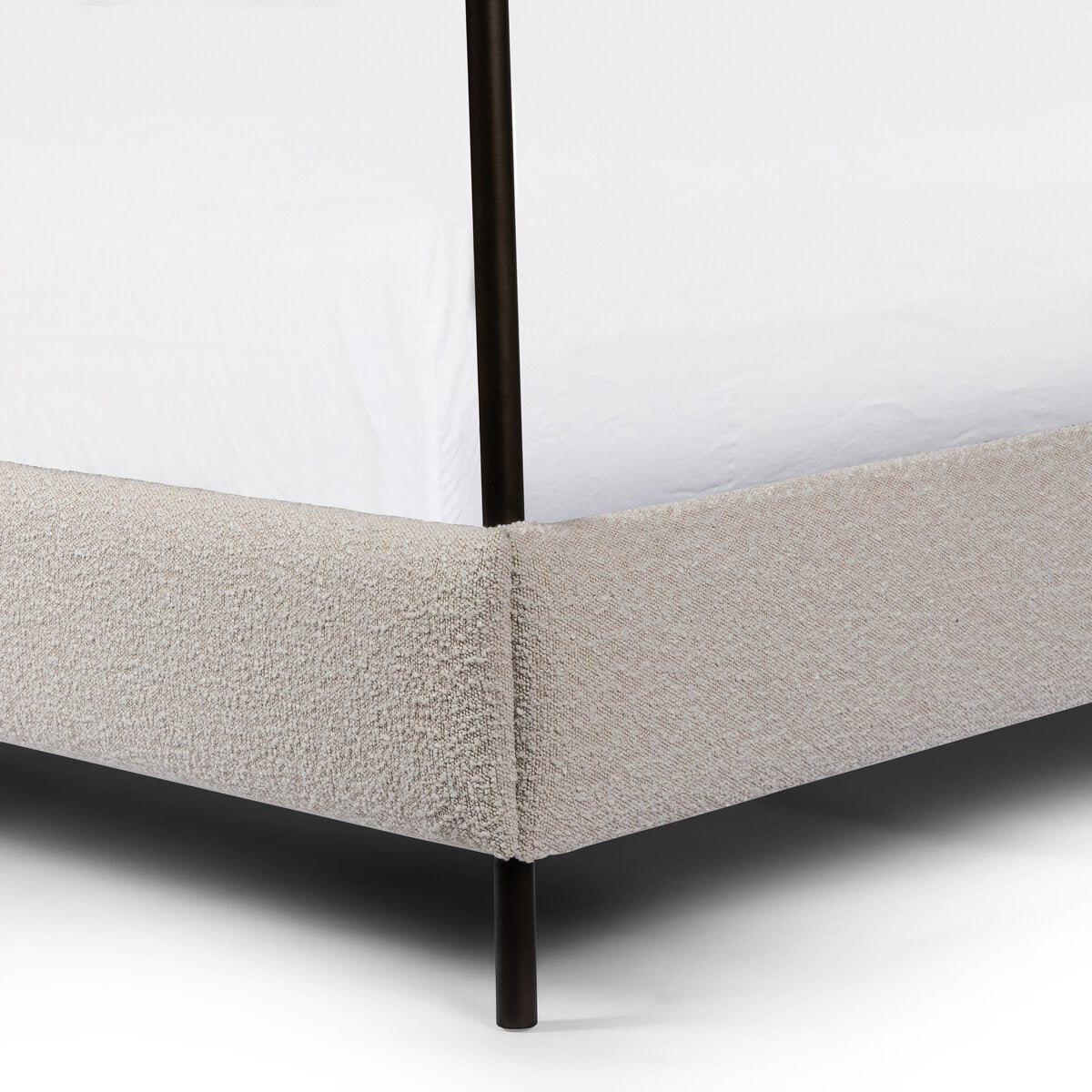 Close-up of a bed with beige fabric and black metal legs on a white background