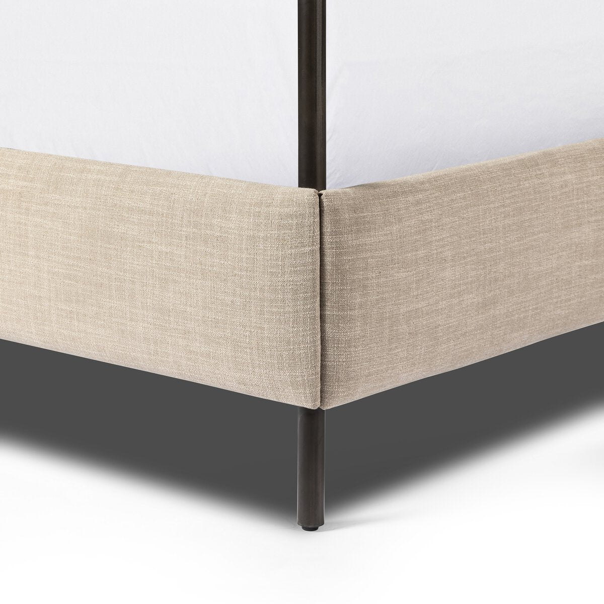 Close-up of a beige upholstered bed frame corner with a black metal leg on a white background