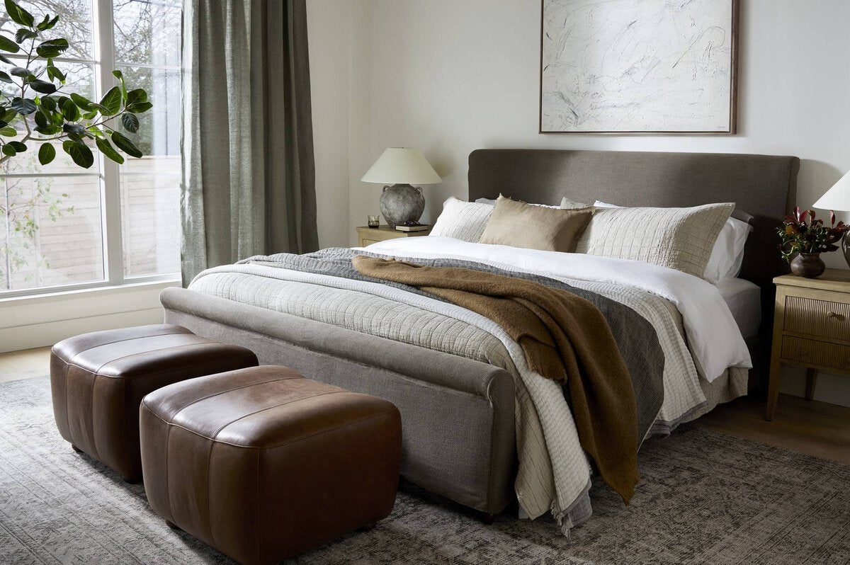 Modern bedroom with a bed, ottomans, and decorative elements.