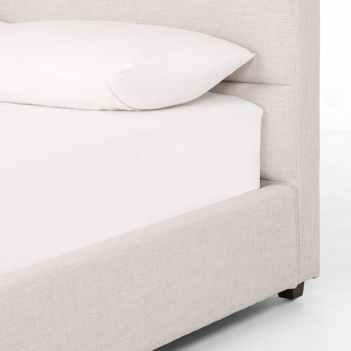 Beige upholstered bed with white bedding on a plain background