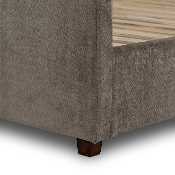 Close-up of a brown upholstered bed frame corner with wooden legs.