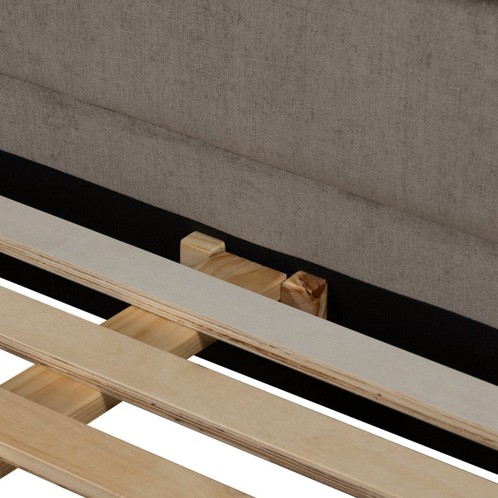 Wooden slats of a bed frame against a gray upholstered headboard.