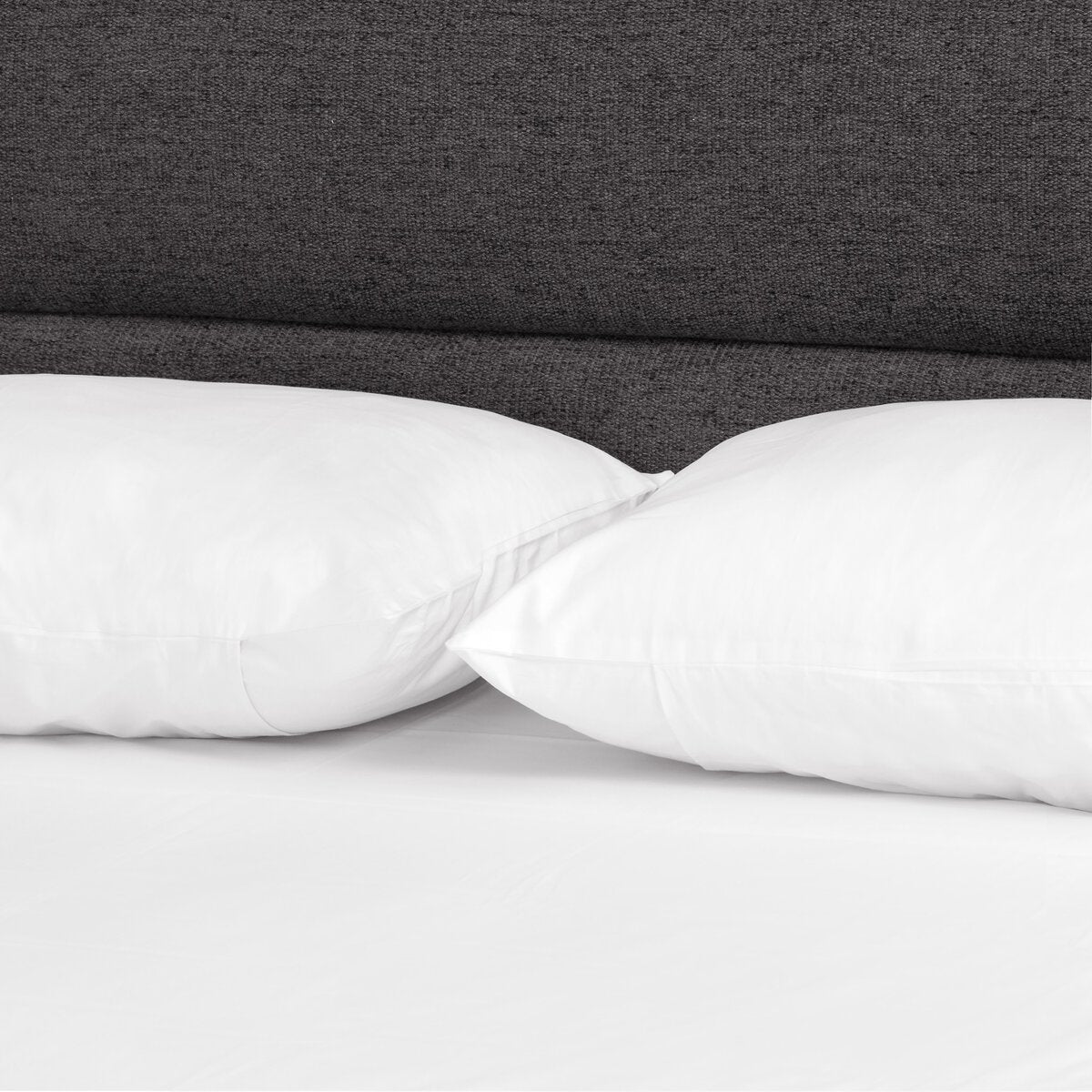 Two white pillows on a bed with a dark gray headboard.