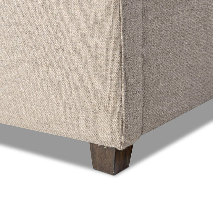 Close-up of a corner of a beige upholstered chair with wooden legs on a white background