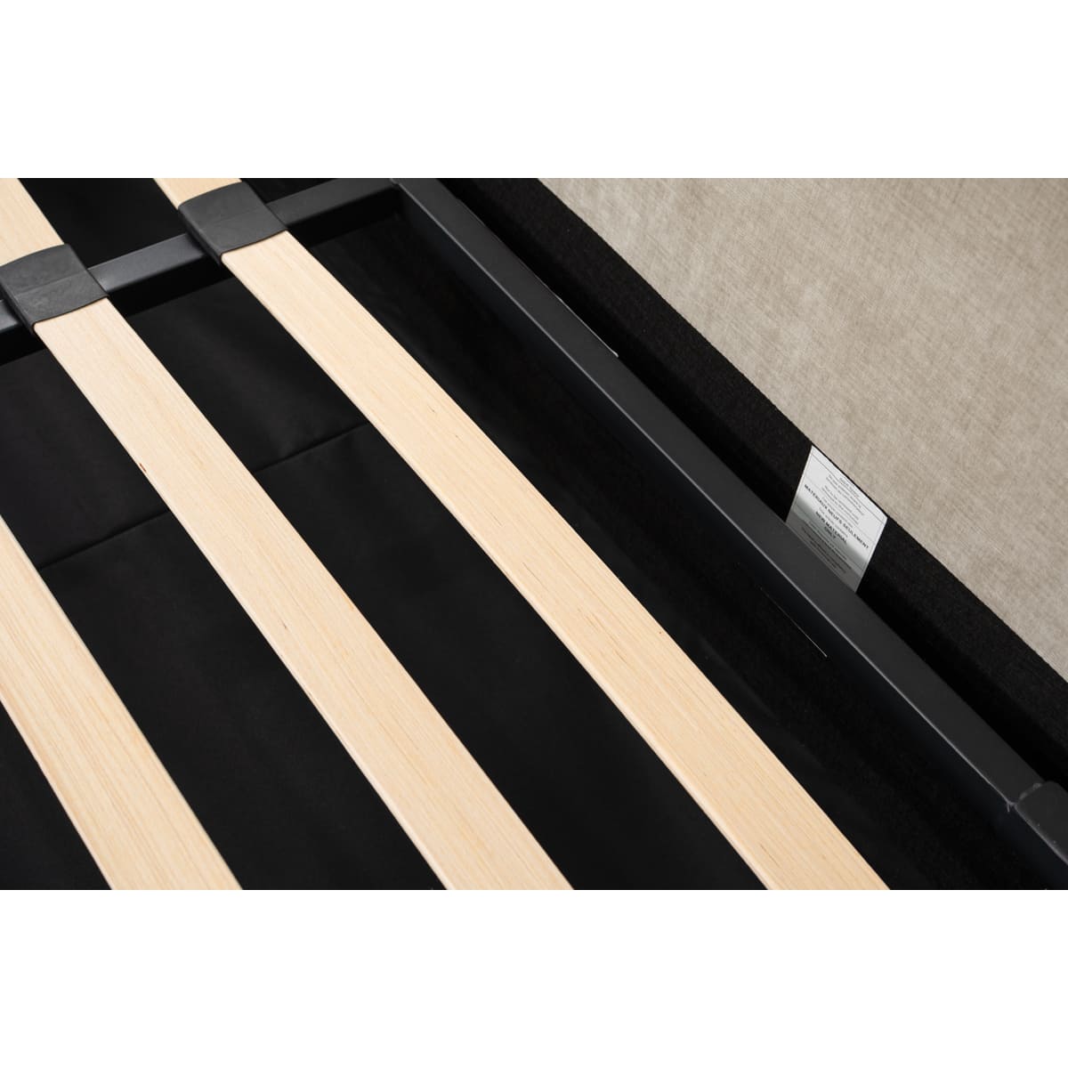 Close-up of a black metal bed frame with wooden slats on a beige carpet.