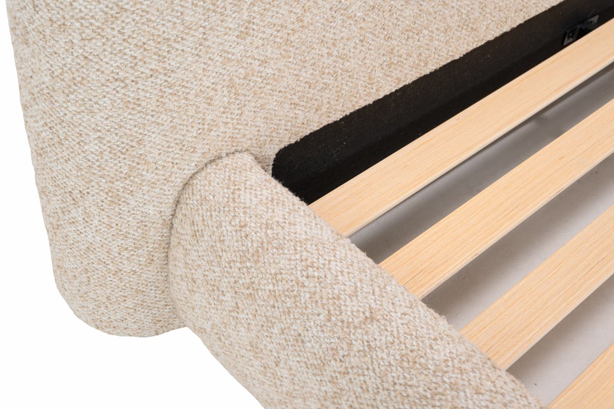 Close-up of a bed frame with wooden slats and beige upholstered headboard.
