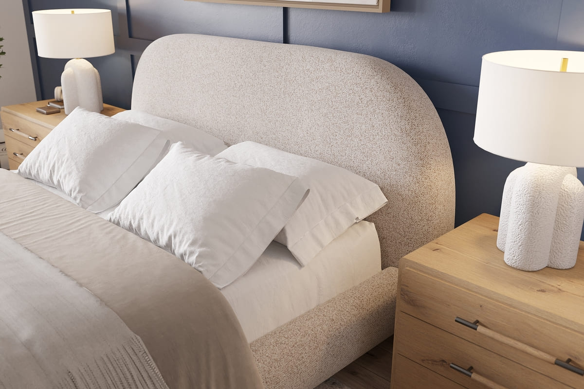 Neatly made bed with pillows and a lamp on a nightstand in a bedroom setting.