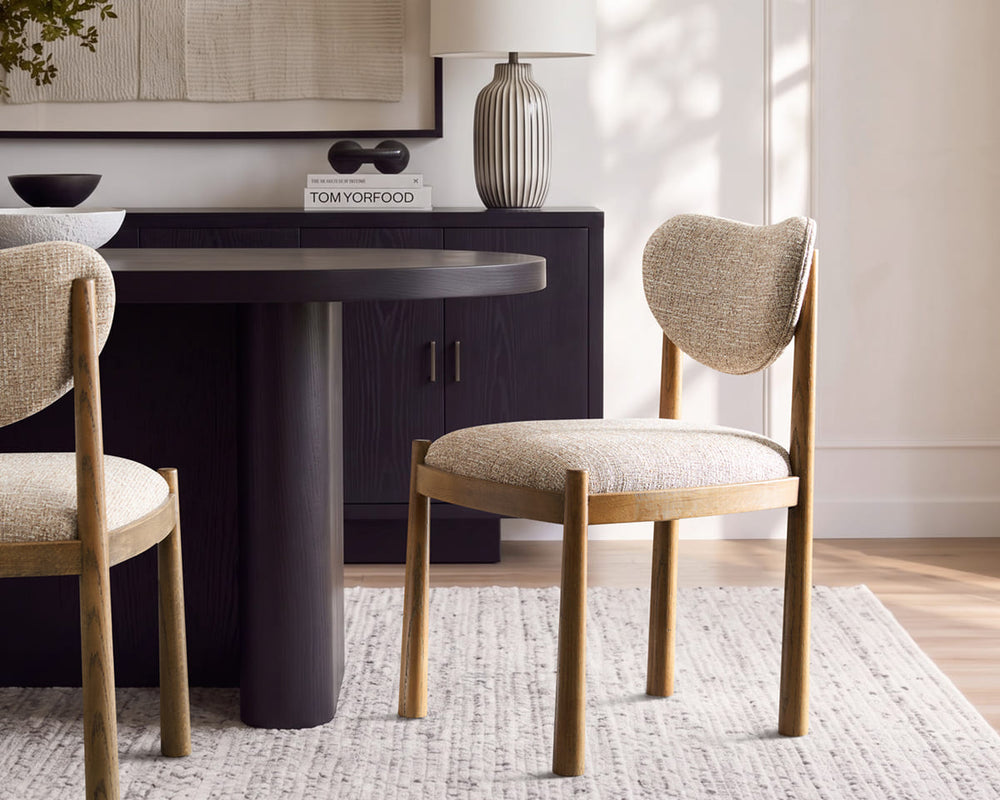 Vela dining chairs with solid oak frames and textured beige upholstery, styled at a dark round table in a modern dining room